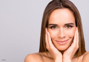 Brunette woman smiling and holding her hands to her cheeks